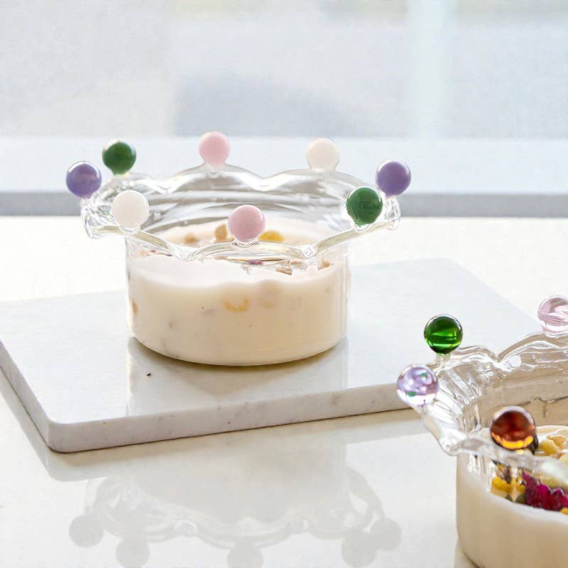 A borosilicate glass serving bowl filled with a fruit yoghurt, sculpted with a dramatic wavy, crown-like rim. The rim is adorned with alternating, colorful solid glass beads (pink, dark green, cream, purple), creating a playful and elegant dessert or candy dish