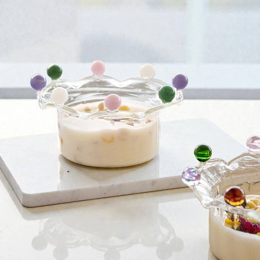 A borosilicate glass serving bowl filled with a fruit yoghurt, sculpted with a dramatic wavy, crown-like rim. The rim is adorned with alternating, colorful solid glass beads (pink, dark green, cream, purple), creating a playful and elegant dessert or candy dish