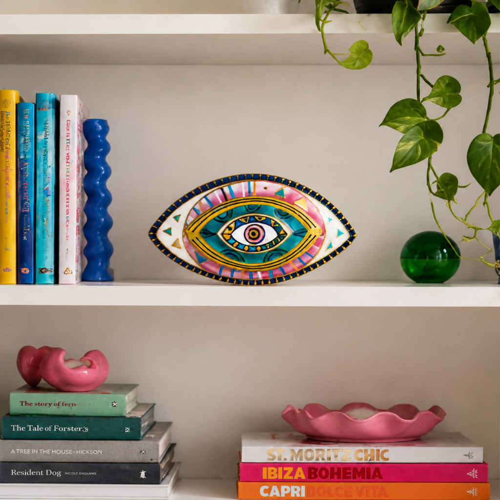 Decorative eye sculpture on a shelf with books and a plant