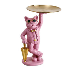 A stylish, matte pink French Bulldog statue leaning casually against a metallic gold umbrella. The dog wears gold-rimmed black sunglasses and a matching gold bow tie, holding a polished gold serving tray high above its head. This functional 'Sassy Soul' sculpture is a perfect maximalist accent for entryways or coffee tables.